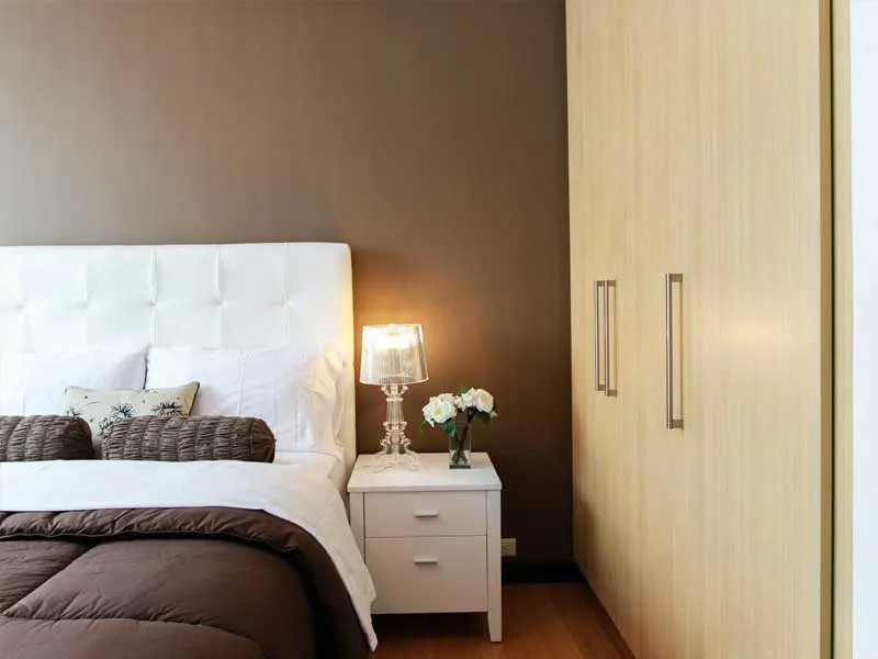 A bright bedroom with a white headboard, bedside lamp and wardrobe